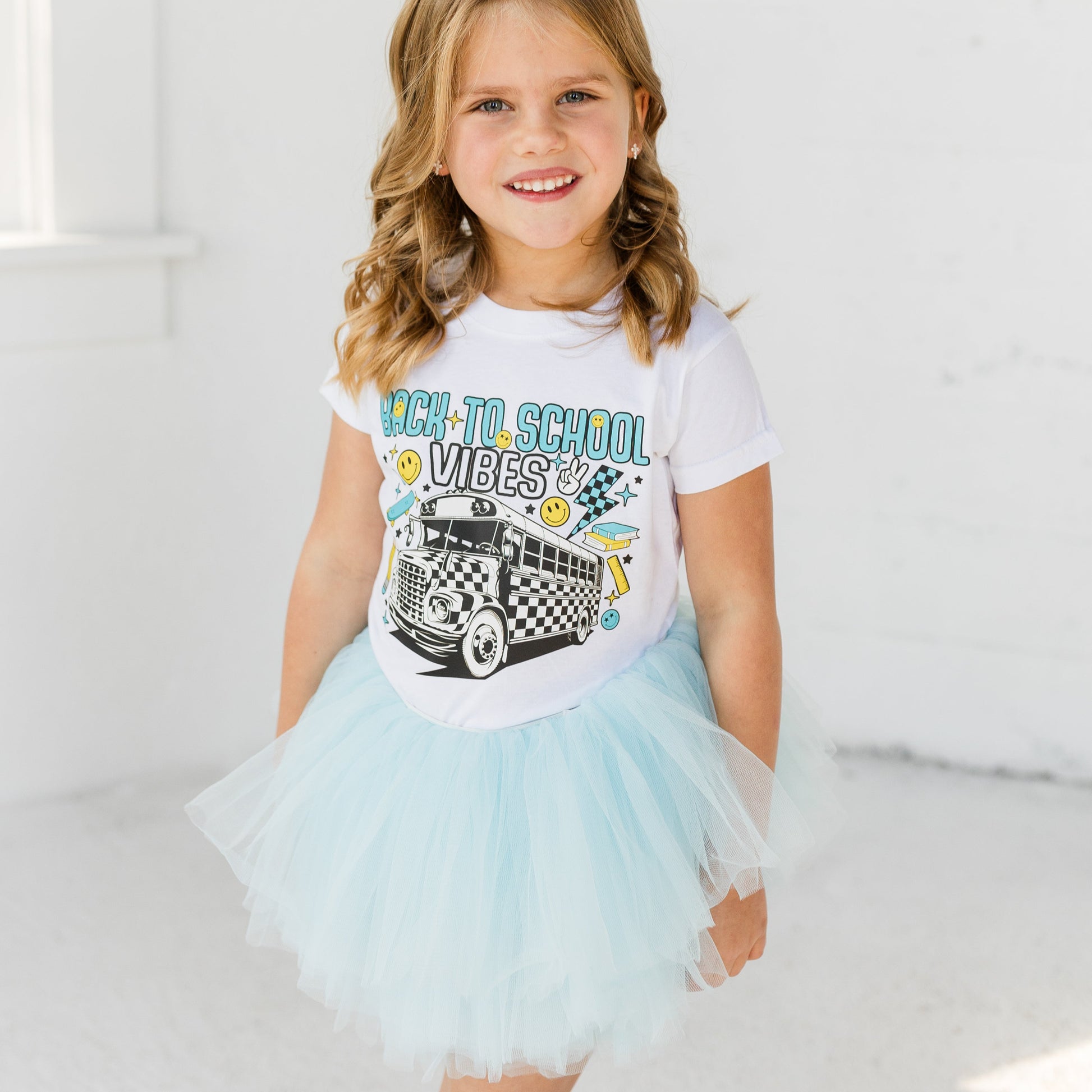 Young girl wearing a white t-shirt with a graphic design and a light blue tutu skirt on a white background.