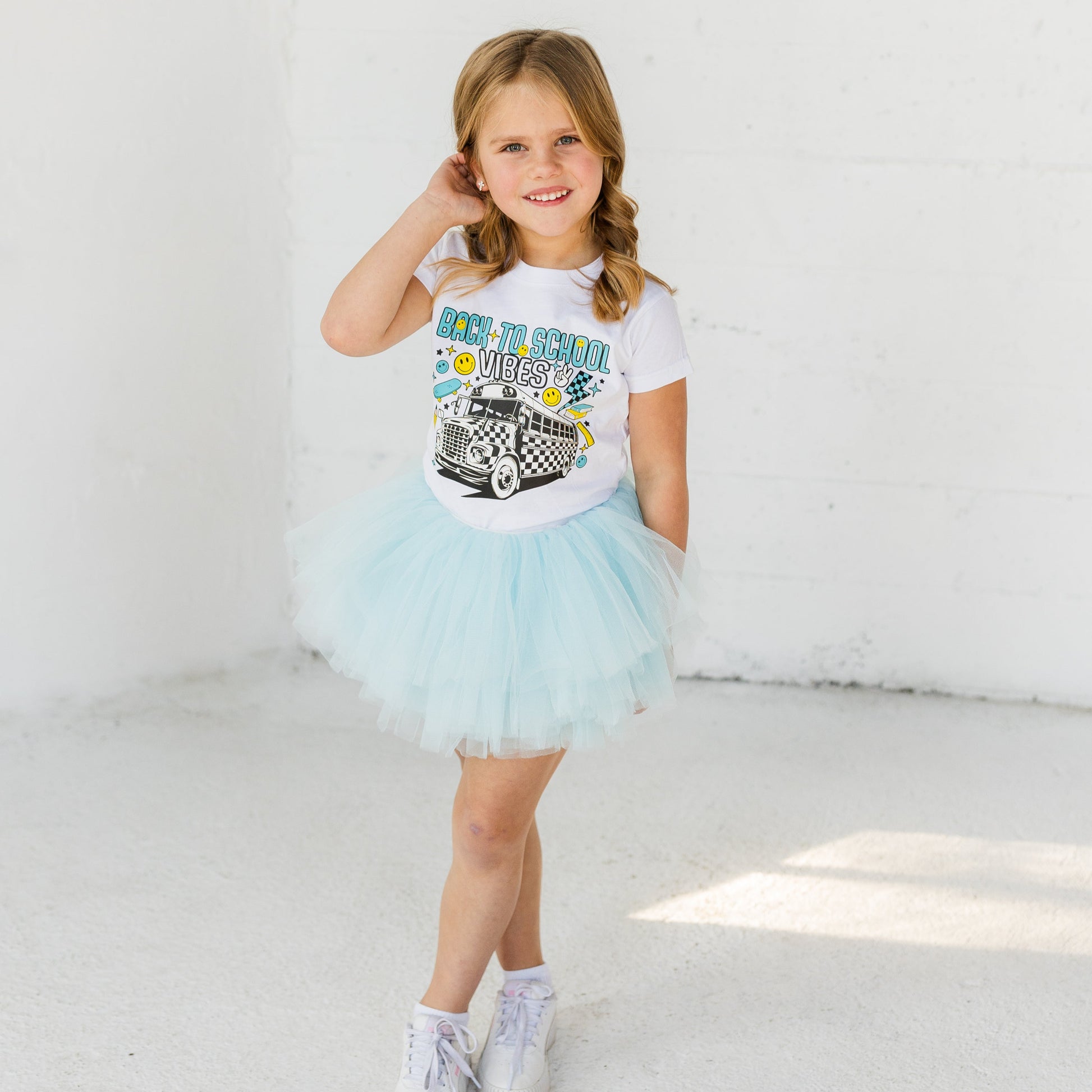 Young girl wearing a white t-shirt with a graphic design and a light blue tutu skirt on a white background