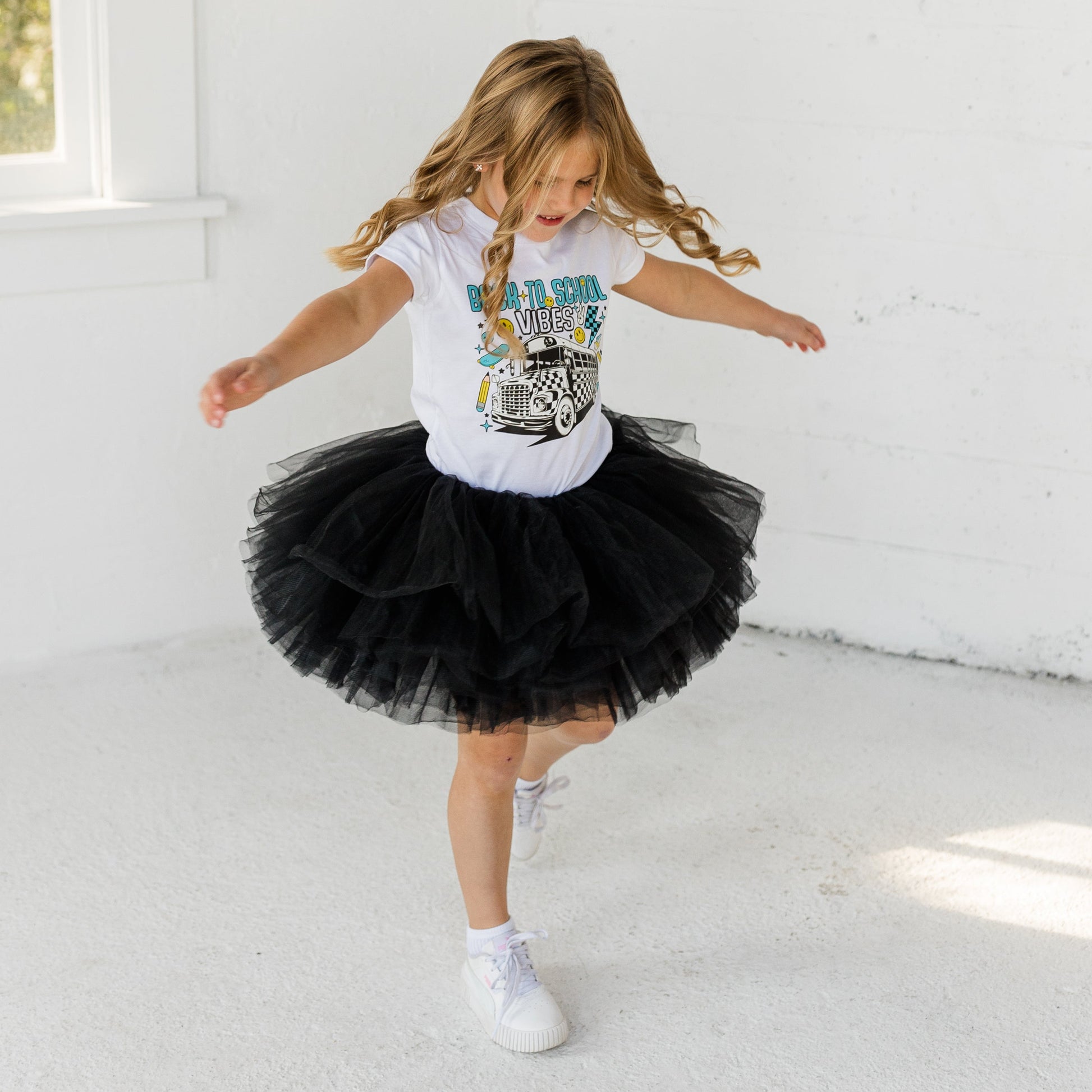 Young girl in a black tutu and white t-shirt dancing in a bright room.