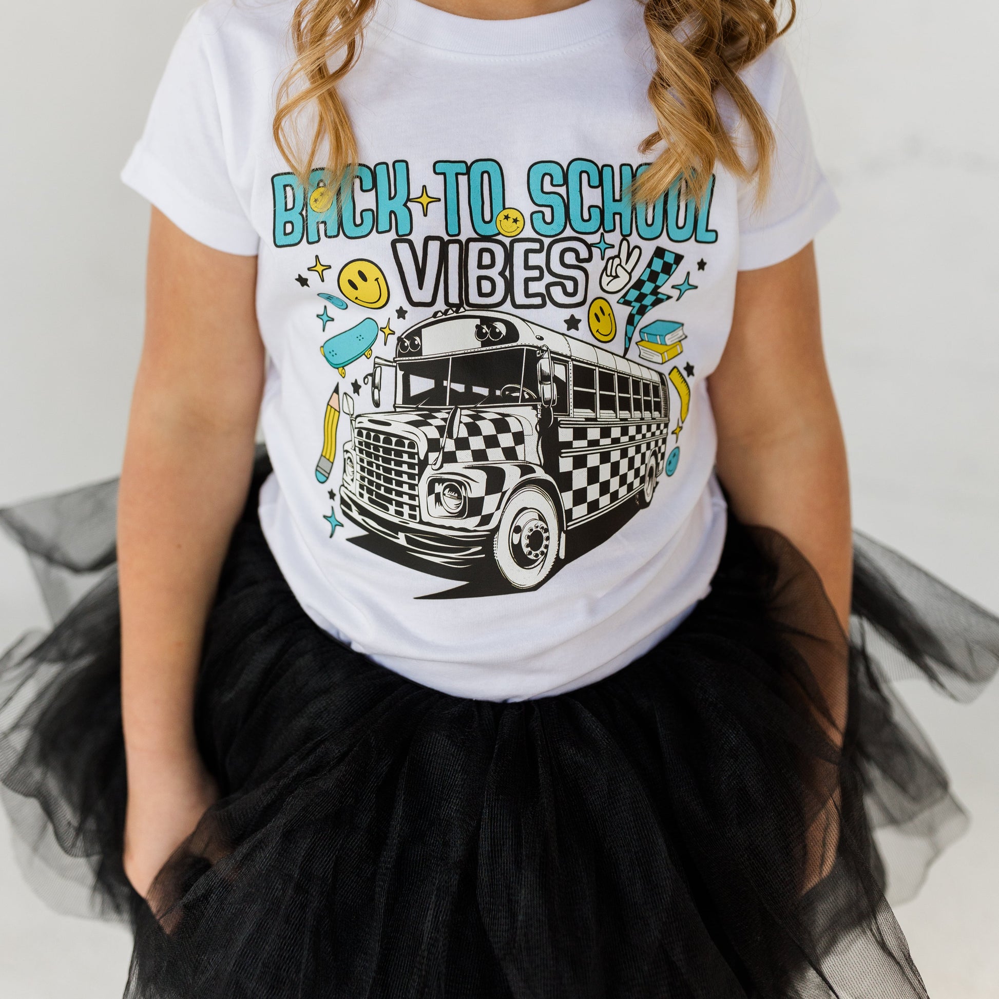 Girl wearing a 'Back to School Vibes' t-shirt with a school bus graphic on a plain background