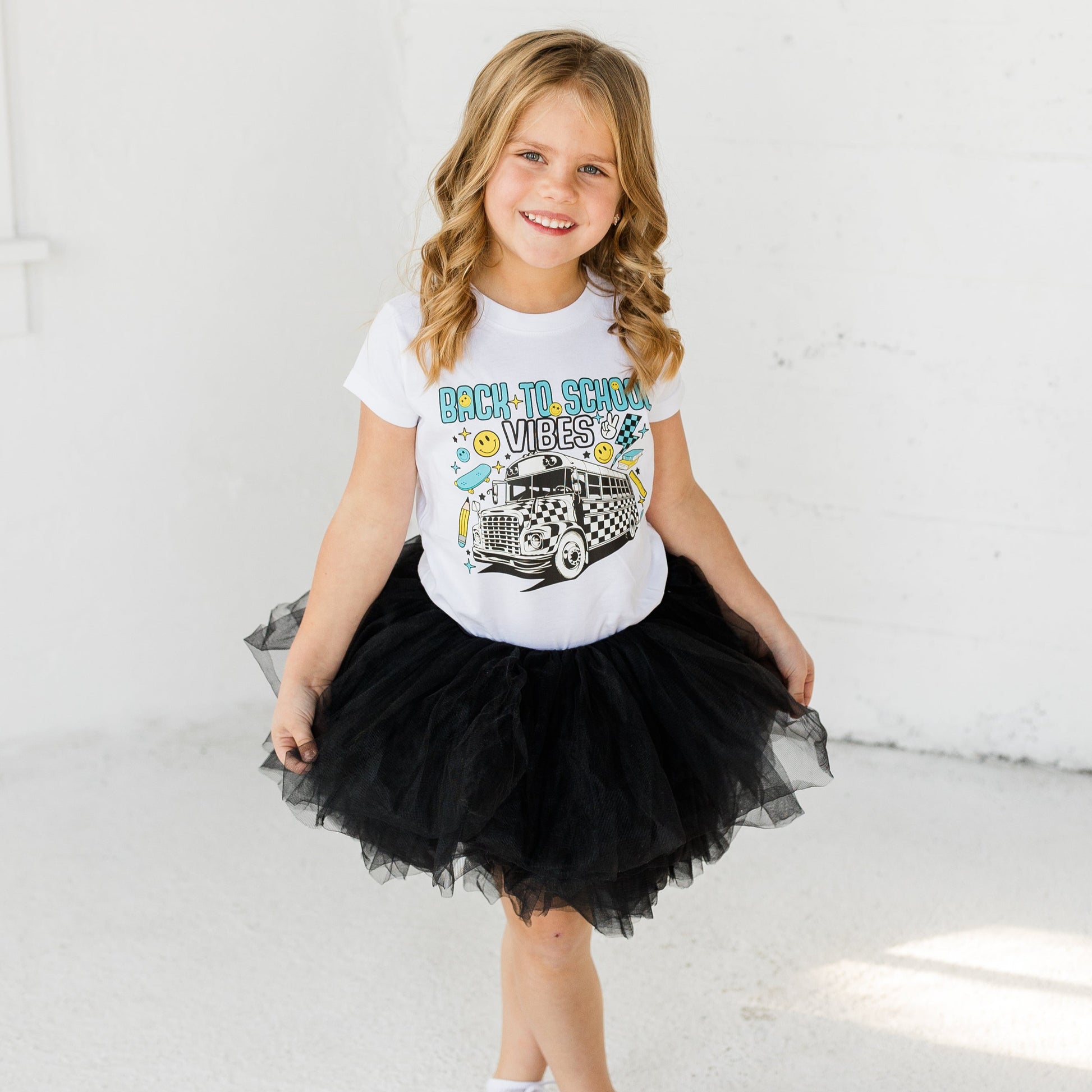 Smiling young girl wearing a white "Back to School Vibes" graphic t-shirt with a black tulle tutu.