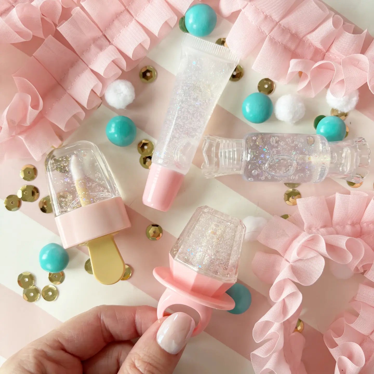 Decorative items including a pacifier, small bottles, and colorful balls on a pink and gold confetti background.