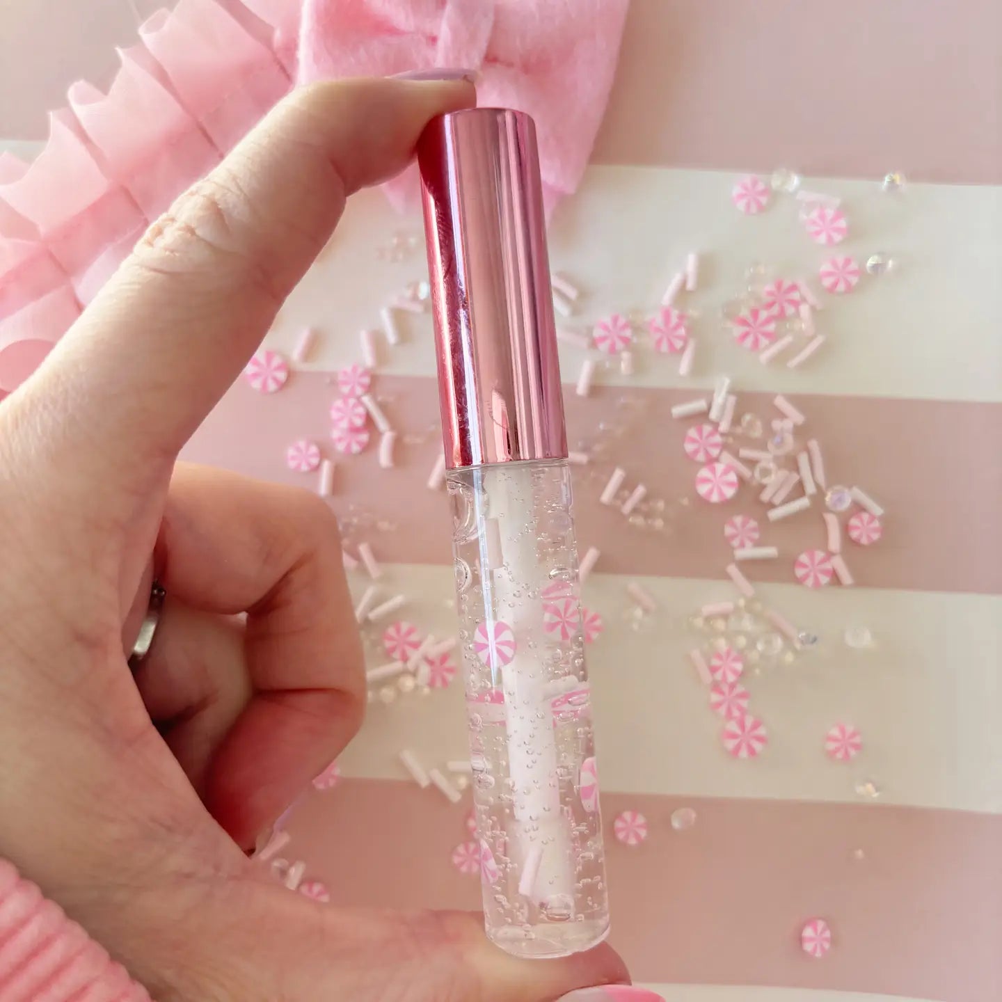 Hand holding a clear bottle with a pink cap against a decorative background