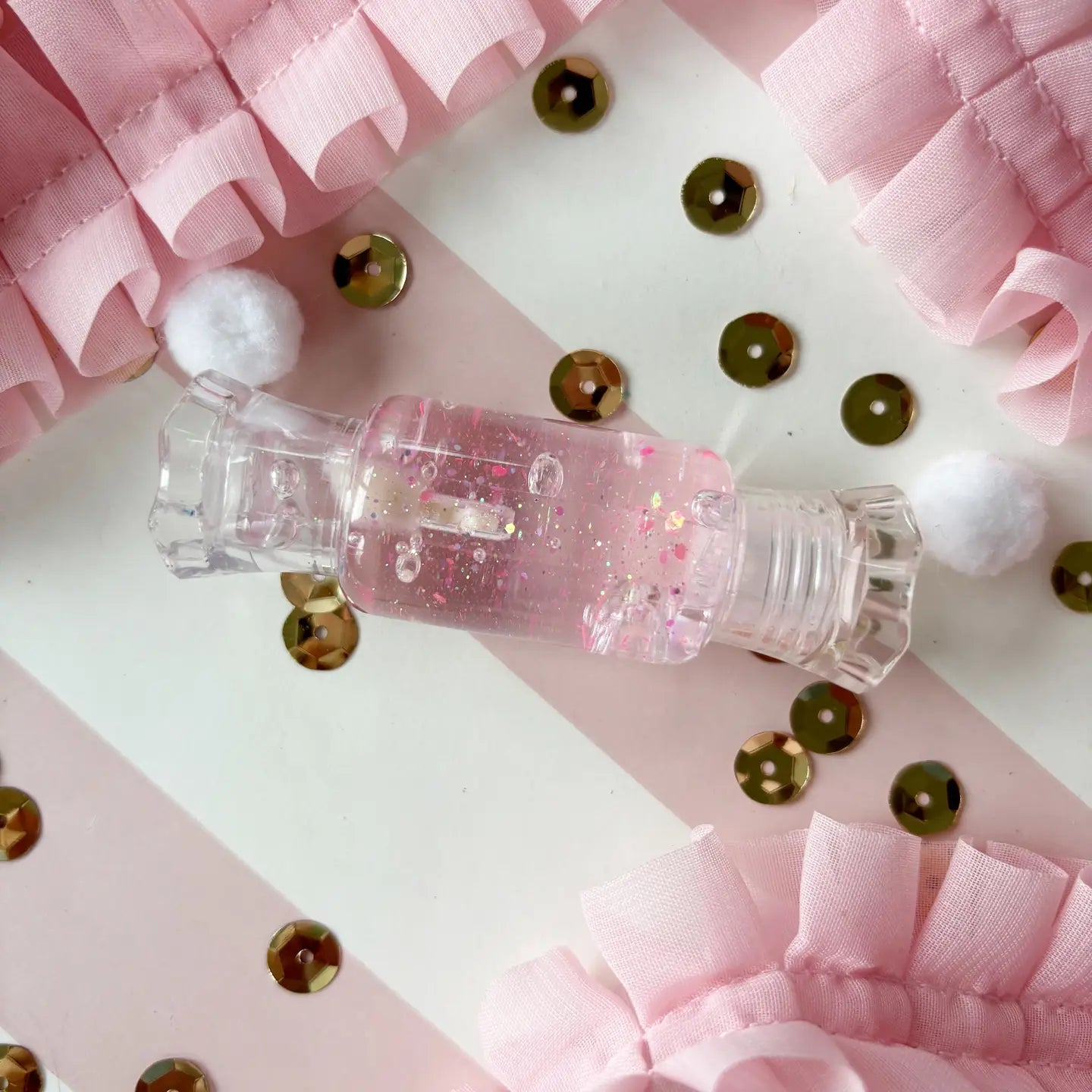 Small pink bottle with glitter on a checkered background with pink ribbons and sequins.