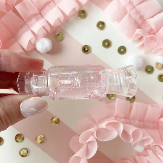 Clear bottle with pink glittery liquid held by a hand against a decorative background
