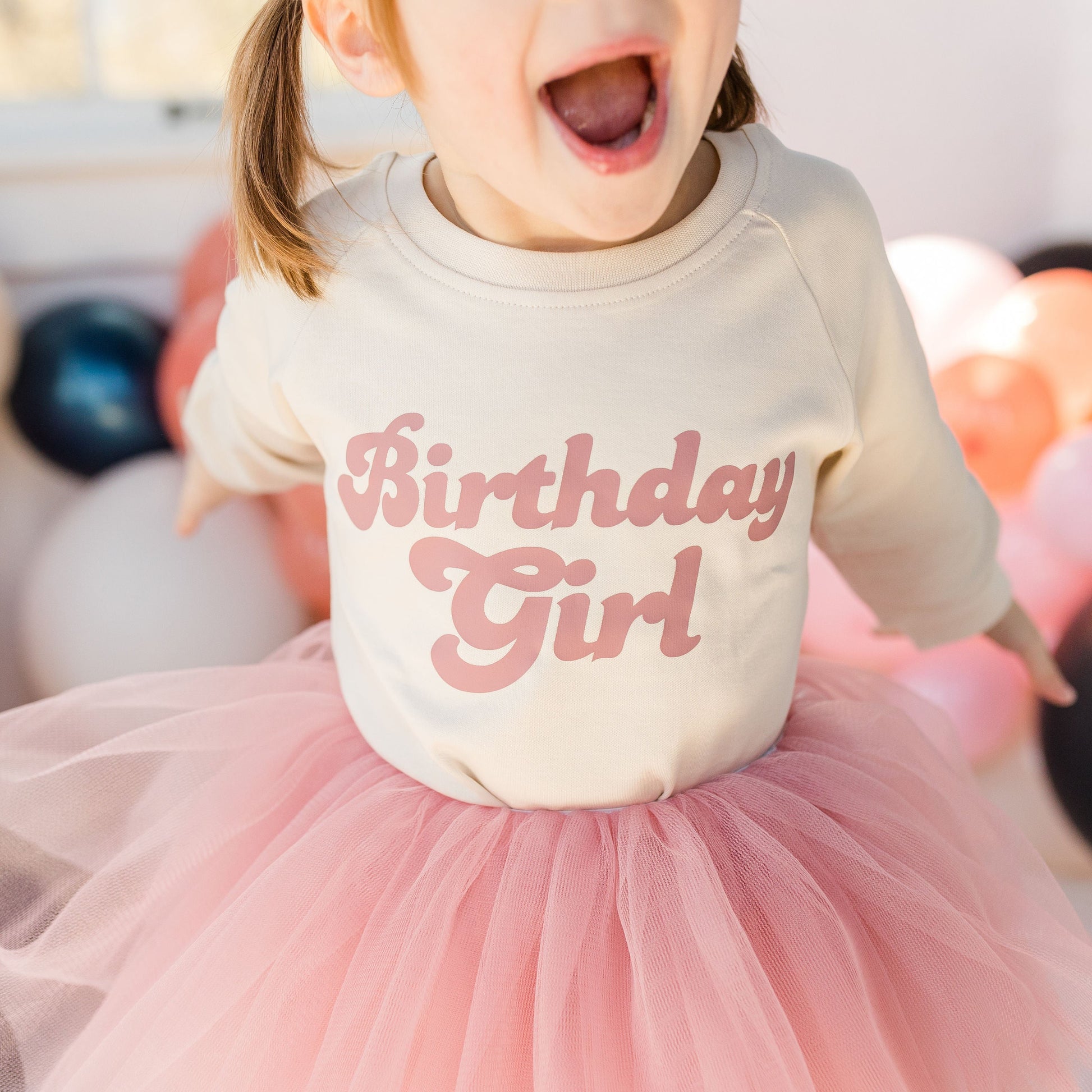 Child wearing a 'Birthday Girl' shirt with balloons in the background