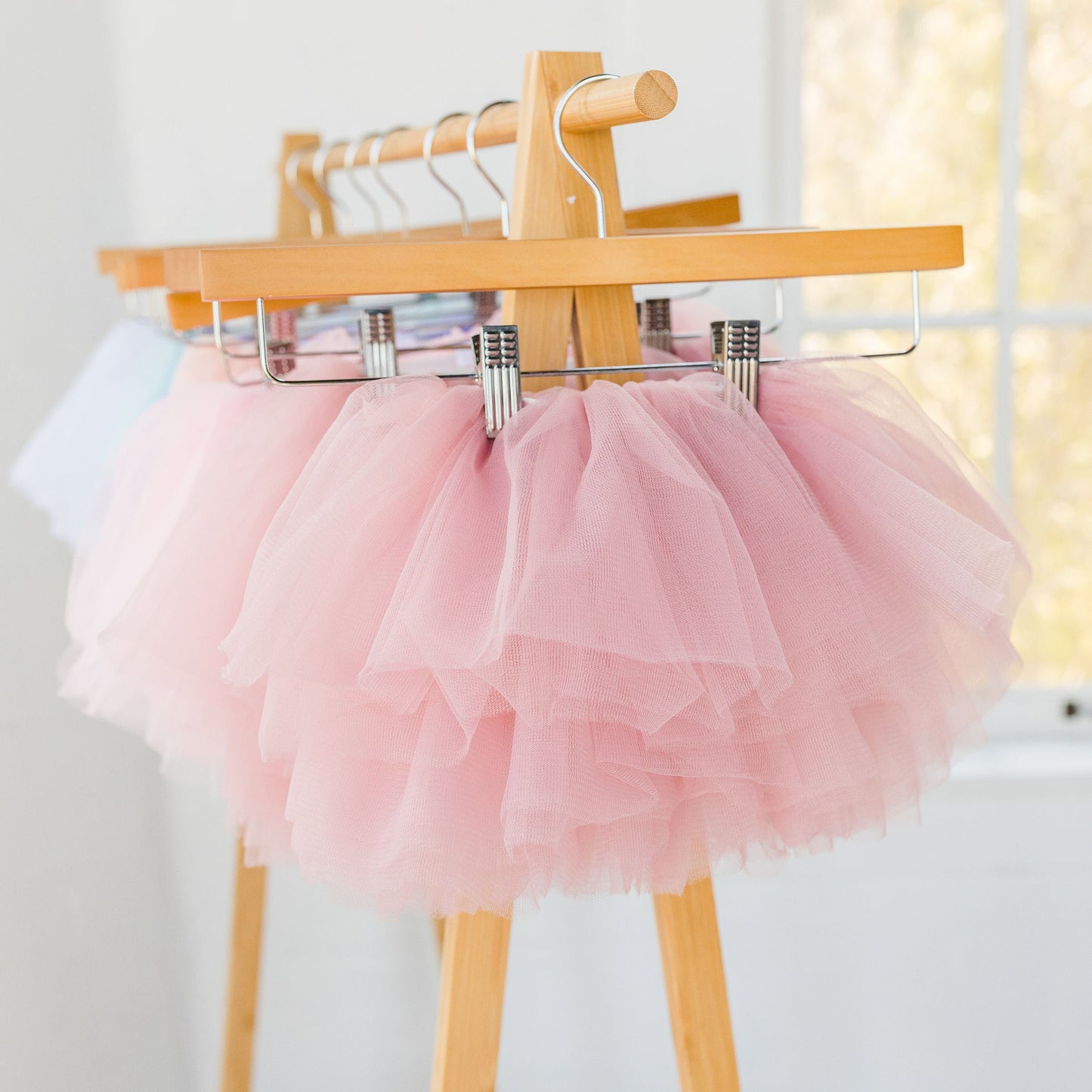 Pink tutu skirt on a wooden hanger against a white wall.