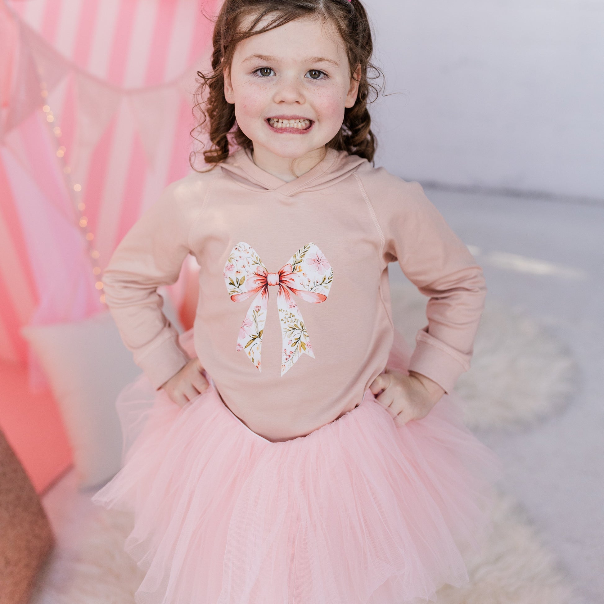Young girl in a pink outfit with butterfly design standing in front of pink balloons.