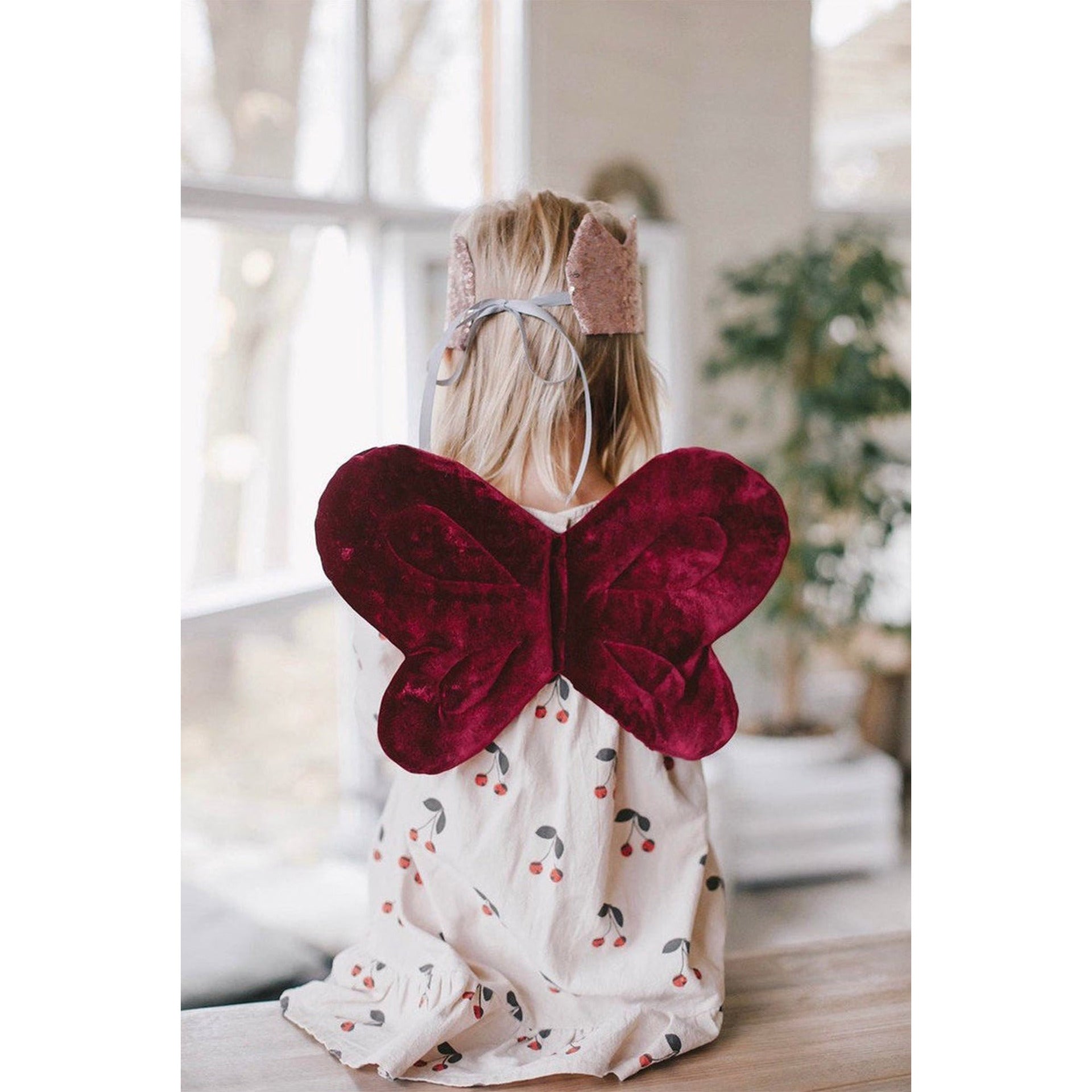 Child wearing red butterfly wings indoors