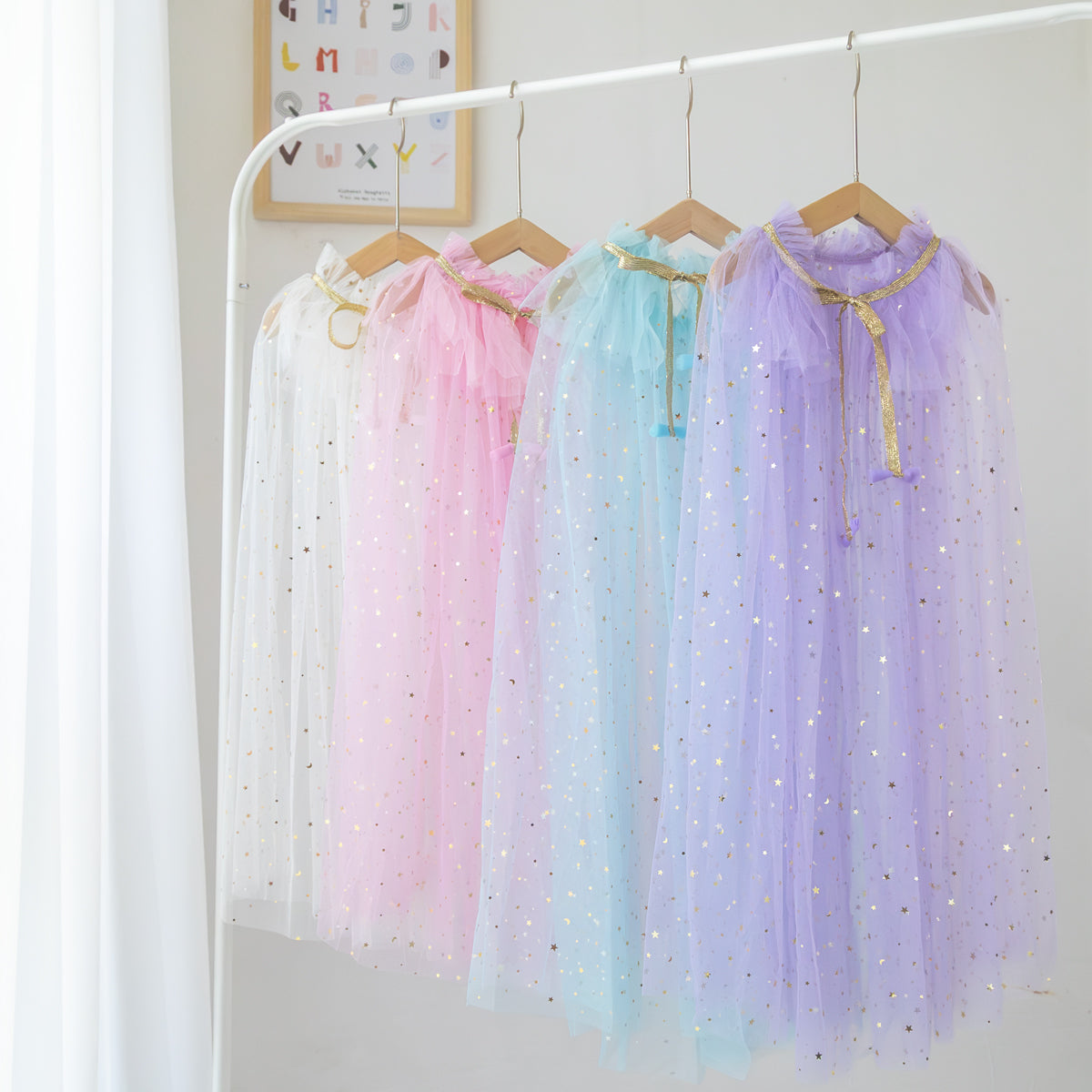 Tulle stary Capes for kids dress up on wood hangers lined up on white clothing bar. 