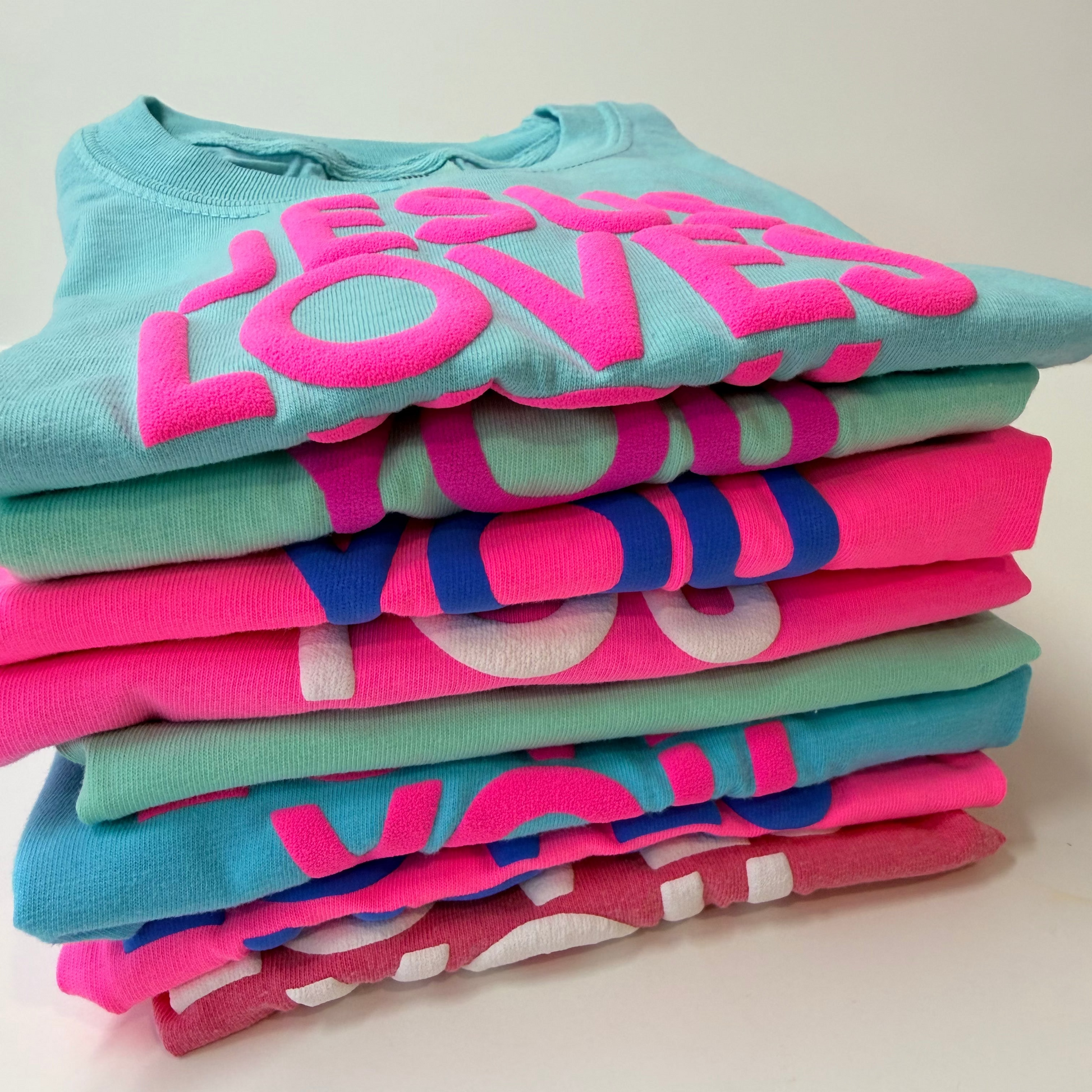 Stack of colorful t-shirts with 'LOVE' printed on them against a light background