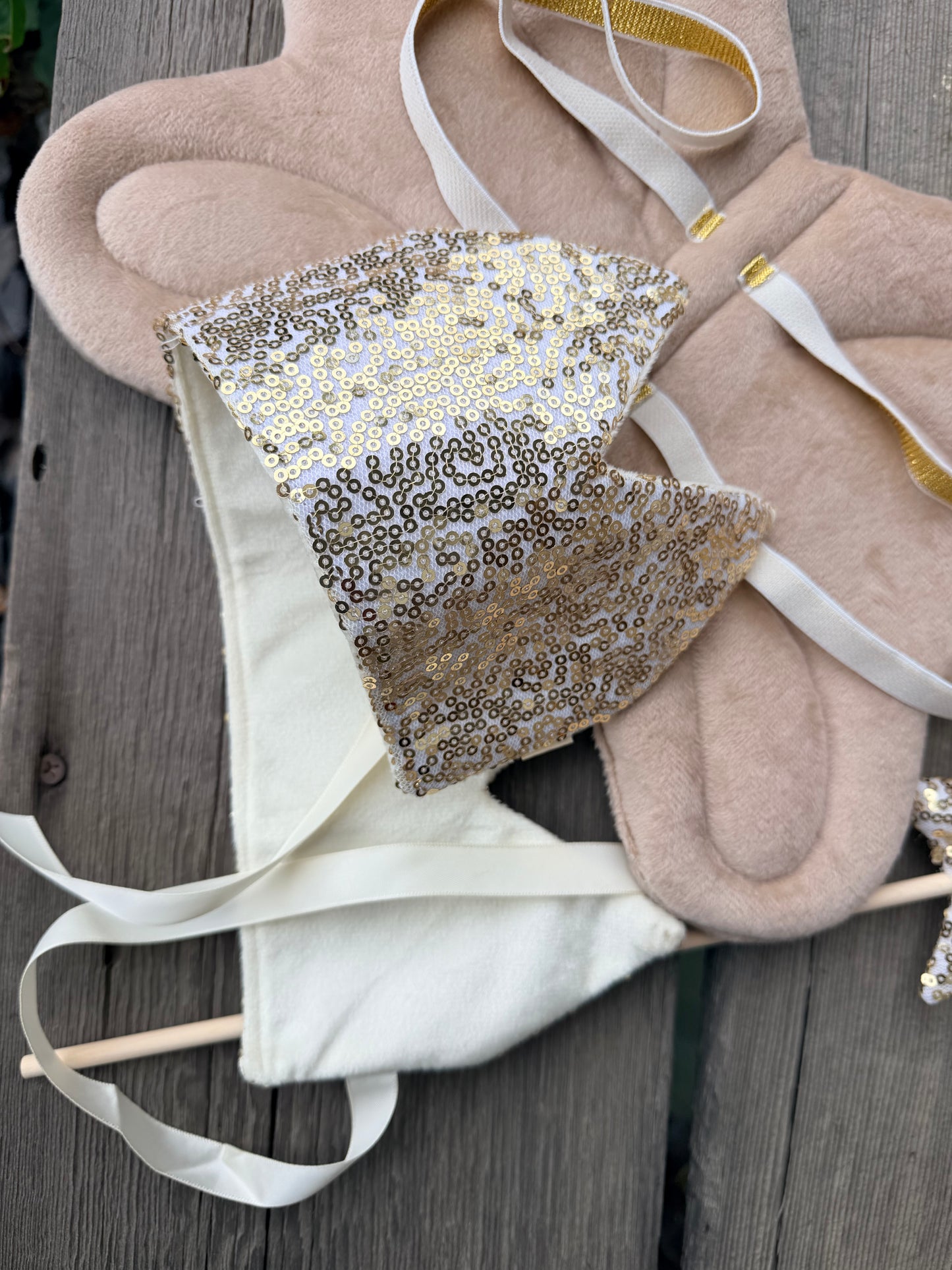 Decorative crown with gold sequin fabric and white ribbons on a wooden surface