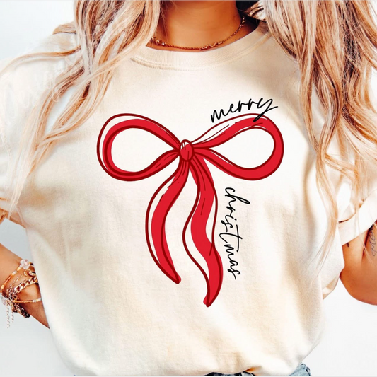 Cream colored t-shirt with large red bow and “Merry Christmas” text in handwritten font.