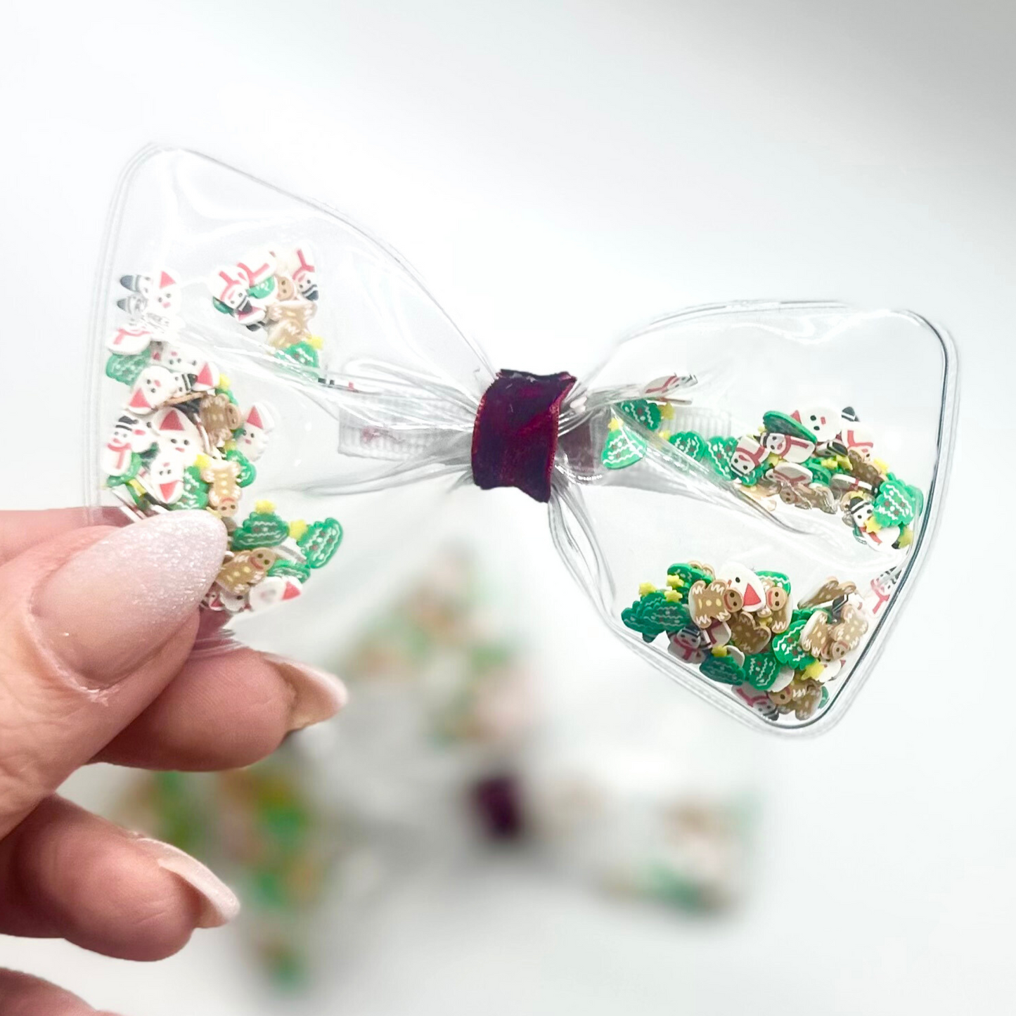 Christmas confetti in clear bow with velvet deep red ribbon center with clip on the back. placed on a white background
