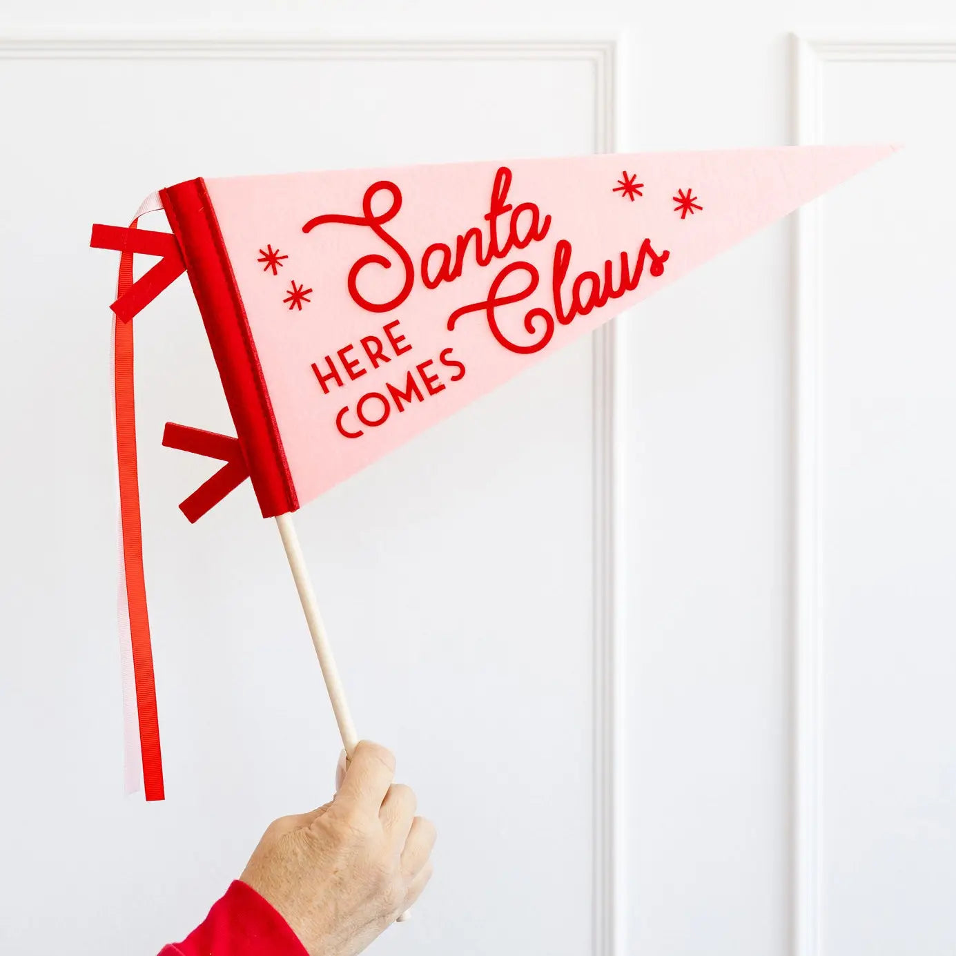 Hand holding a red flag with 'Santa Claus Here Comes' text against a white background