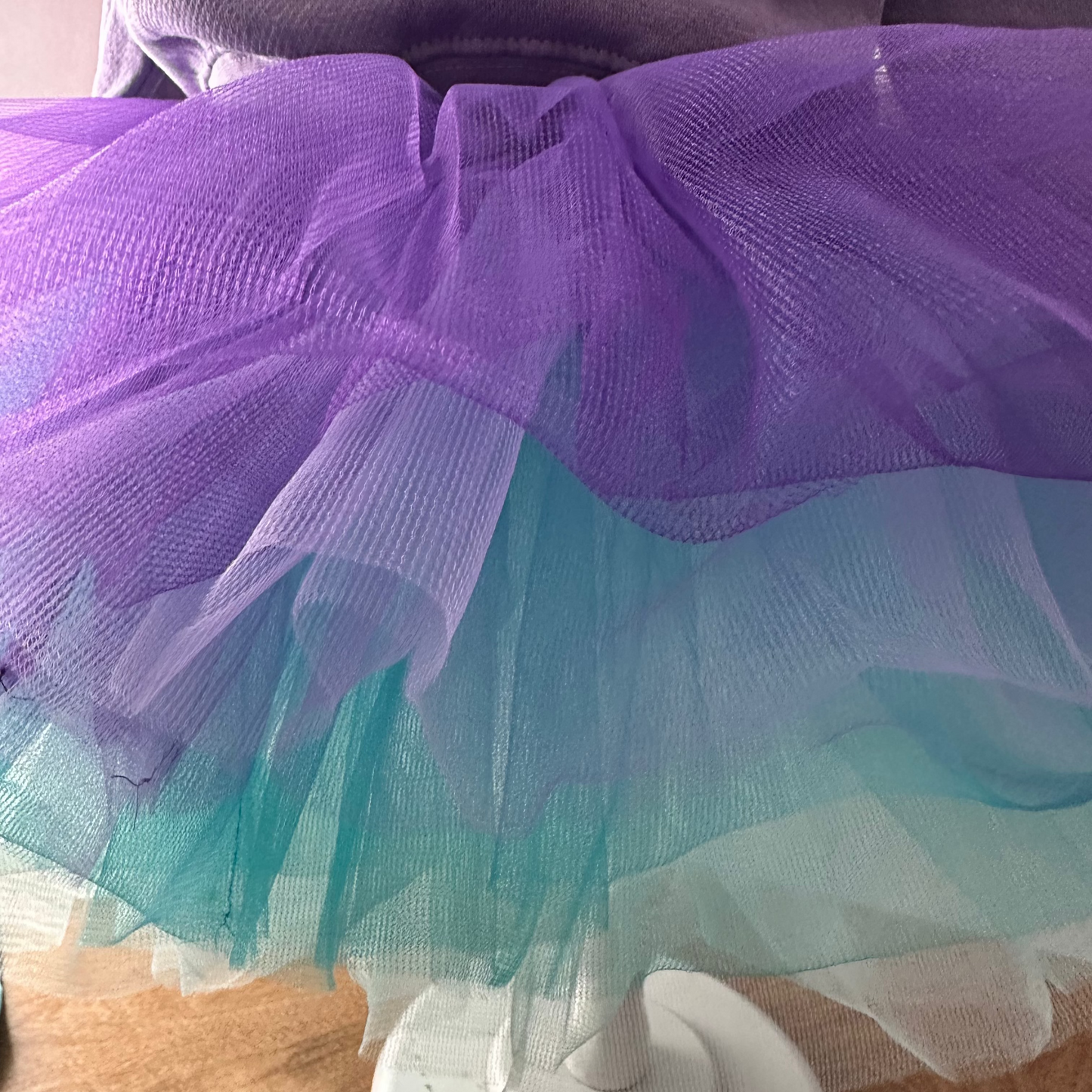 Purple and teal tutu on a mannequin stand with a wooden floor background