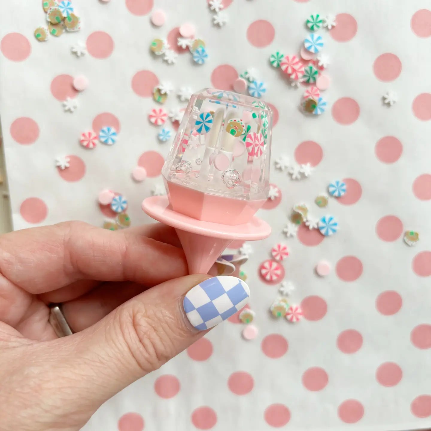 Small decorative item held by a hand with checkered nail polish on a polka dot background