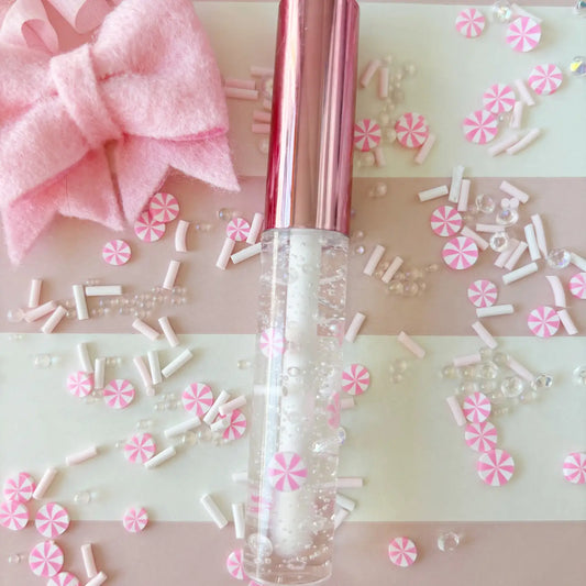 Clear lip balm with pink cap on a decorative background with pink and white candy-like decorations.