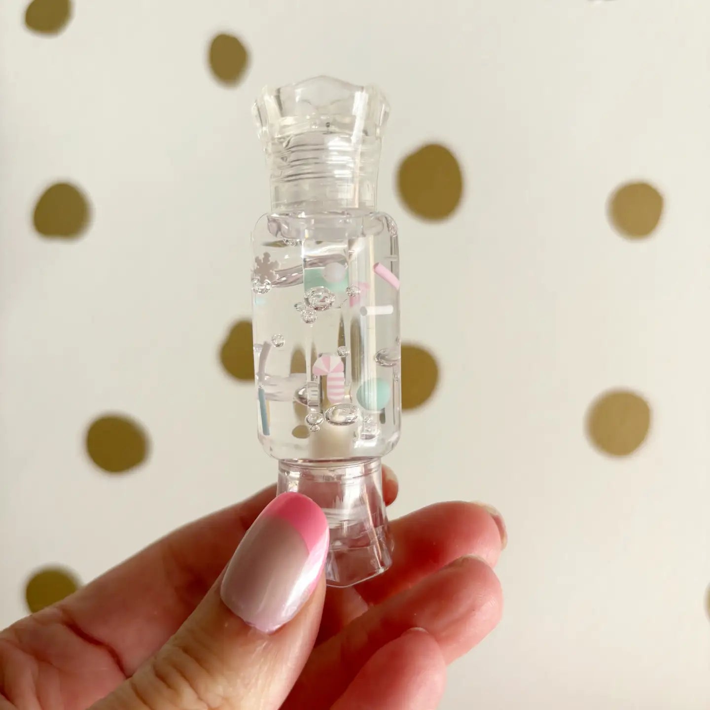Clear plastic bottle with floral designs held by a hand against a polka dot background