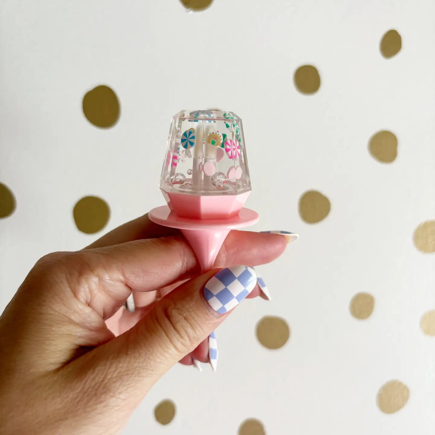 Hand holding a small decorative item with floral design against a polka dot background