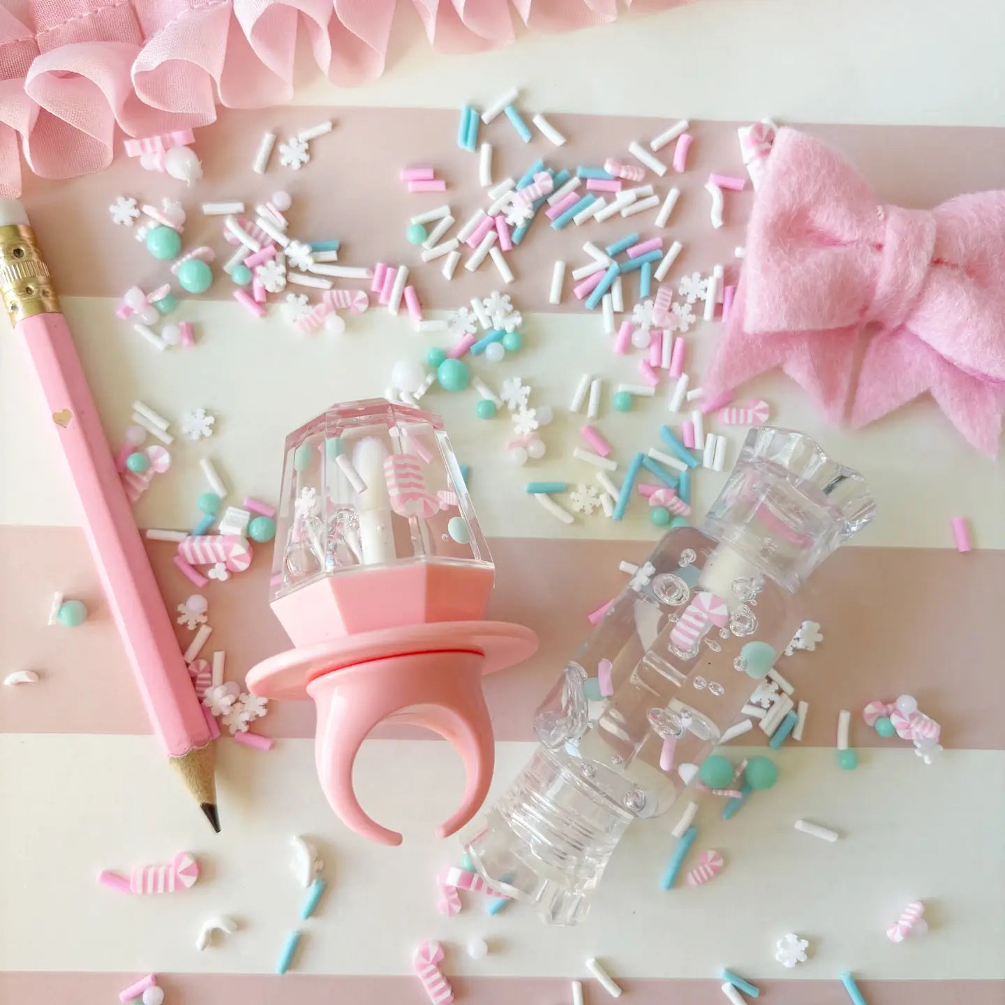 Pink pacifier, pencil, and decorative items on a pink and white striped background